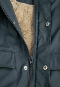 Granatowa wodoodporna kurtka z beżowym polarem wewnątrz, z zapięciem na zamek błyskawiczny i napy. Posiada boczne kieszenie oraz gładką, teksturowaną zewnętrzną warstwę.