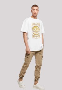 White short-sleeve t-shirt featuring a gold "Hakuna Matata" graphic, paired with khaki cargo pants, and white sneakers.