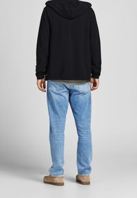 Black hooded sweatshirt with long sleeves, paired with light blue jeans. The fabric appears soft; the fit is relaxed with visible pockets.