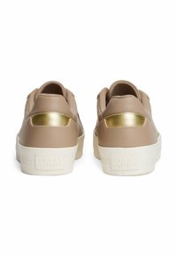 Baskets en cuir beige avec des accents dorés et des languettes texturées, présentant une semelle blanche et un logo en relief sur le talon.