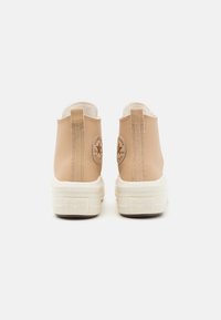 Beżowe trampki Converse All Star mają gładką cholewkę, dwa uchwyty oraz grubą białą podeszwę z wytłoczonym logo na pięcie.