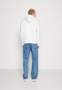 Hellgrauer Kapuzenpullover mit flachem Kordelzug, kombiniert mit lockeren blauen Jeans aus Denim mit Gesäßtaschen und einem Markenetikett.