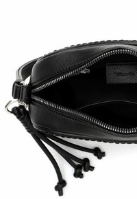 Musta nahkainen käsilaukku, jossa on vetoketjusuljenta, yläreunassa punottu kuvio ja koristeelliset hapsut nahkanauhoista.