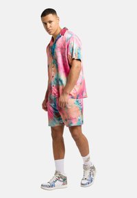 Kortermet, flerfarget skjorte og shorts sett laget av lett materiale, med levende mønstre i rosa, blå og ferskenfarger.
