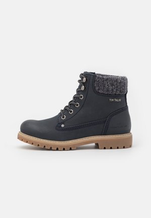 Boots bleu foncé à semelle beige, avec lacets à l'avant et bord-côte gris, marqué "Tom Tailor" sur le côté.