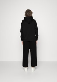 Czarna bluza z dużym kapturem i długimi rękawami, połączona z luźnymi czarnymi spodniami. Noszona z białymi trampkami, strój ma swobodny charakter.