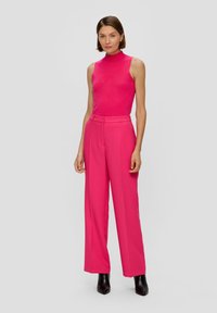 Fitted, mouwloos roze top gecombineerd met wijde roze broek. Glad materiaal met een geribbelde textuur. Zwarte hoge laarzen maken de look compleet.