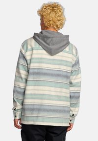 Chaqueta de camisa a rayas para hombre en verde claro, beige y gris. Cuenta con una capucha gris y puños con botón. Textura suave con un corte relajado.