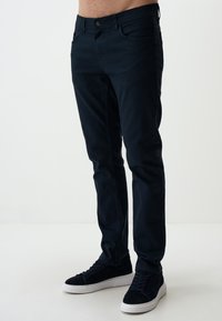 Ciemnoniebieskie dżinsy slim fit z bawełnianej tkaniny o gładkiej fakturze, z przednimi kieszeniami i standardowym zapięciem na guzik. Połączone z czarnymi sneakersami.