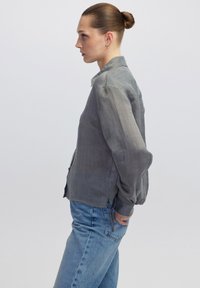Camicia grigia con bottoni, caratterizzata da un motivo a righe textured, con colletto e maniche lunghe, abbinata a jeans azzurri chiari.