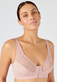 Sujeta sin aros acolchada en suave tela rosa con superposición de encaje floral. Presenta bordes en forma de ola y un cierre delantero para poner y quitar fácilmente.