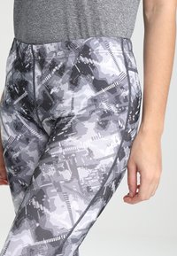 Legginsy wysokiej talii w szarym kamuflażu, charakteryzujące się gładką teksturą i kontrastowymi czarnymi szwami po bokach.