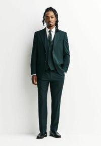 Donkergroen drie-delige pak met een notch lapel, wit overhemd en een stippelstrik. Glanzende zwarte schoenen; gladde textuur met een op maat gemaakte pasvorm.