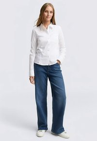 White button-up shirt with a collar, paired with loose-fitting dark blue jeans and white sneakers. Smooth fabric, casual design, relaxed fit.