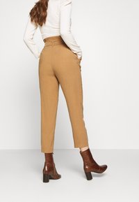 Beige högmidjade byxor med en avsmalnande form, sidfickor och bakknappsningsdetalj, kombinerat med bruna läderstövlar med krokodilskinnsmönster.