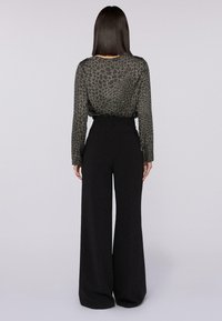 Czarne spodnie z szerokimi nogawkami w połączeniu z przezroczystą, ciemnozieloną bluzką z geometrycznym wzorem i długimi rękawami, widok z tyłu.