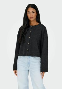 Maglione grigio, accorciato, con bottoni, realizzato in lana di tessuto testurizzato. Presenta un collo rotondo e maniche lunghe con polsini larghi.