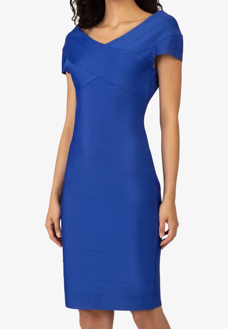 Femme portant une robe bleu roi ajustée, longueur genou, à manches courtes et encolure en V avec une texture horizontale style bandes."