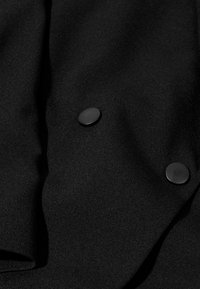 Primo piano di tessuto nero con due grandi bottoni opachi neri cuciti sopra.