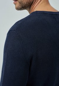 Maglione lavorato a maglia blu navy con tessuto testurizzato, caratterizzato da un collo tondo e maniche lunghe, mostrato da dietro a un angolo.