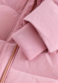 Ružový puffr jacket s tónovým vreckom s embosovaným písmom, hladkou textúrou a kontrastným medeným zipsom.