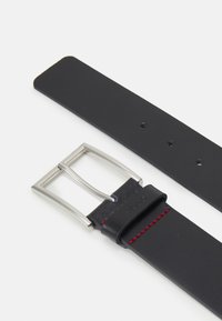 Zwarte leren riem met een zilveren rechthoekige gesp, voorzien van rode stiksels langs de rand en meerdere verstelgaten.
