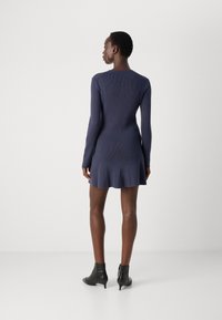 Marineblauw geribd gebreid jurkje met lange mouwen, uitlopende zoom en een fitted silhouet. Draagt met zwarte enkellaarsjes.