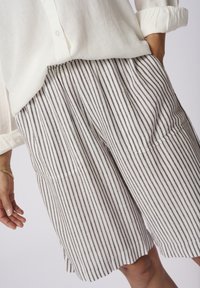 Striped shorts in light beige and dark brown, made of soft fabric. Features an elastic waistband and two front pockets.