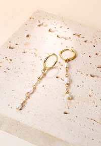 Pendientes de aro de oro con cintas colgantes que presentan perlas blancas. El metal tiene un acabado brillante, con una superficie texturizada que conecta las perlas.