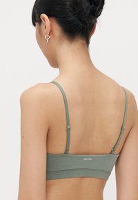 Grüne Bralette mit verstellbaren Trägern, aus weichem Stoff gefertigt, mit schlichtem Design und Logo auf dem Rückenteil.