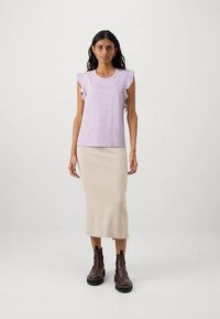 Top de rayas moradas claras con mangas con volantes, combinado con una falda beige ajustada y botines marrones con suelas gruesas.