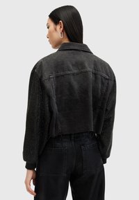 Kuttet svart denimjakke med ensfarget bakside og teksturerte, utsmykkede ermer. Klassisk krage, knappelukking og avslappet passform.