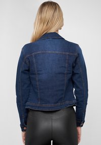 Veste en denim bleu foncé au design ajusté, avec un col pointu, des détails de boutons sur les manches et un dégradé sur les bords.