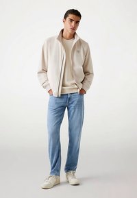 Beežist lukuga jakk helekollase kampsuni kohal, kombineeritud helesiniste teksade ja valgete tossudega. Lihtne, vabaaja disain lõdva istuvusega.