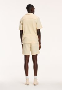 Light yellow waffle-textured shirt with a collar, paired with matching shorts. The outfit features short sleeves and a pocket on the shorts.