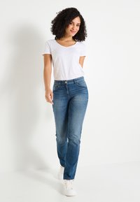 Jean en denim bleu moyen, coupe droite, avec une fermeture à boutons et un design classique à cinq poches, associé à un t-shirt blanc uni à manches courtes.