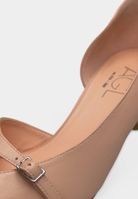 Μπεζ δερμάτινο παπούτσι Mary Jane με ασημένια αγκράφα και χαμηλό τακούνι, με εμφανές το εσωτερικό σήμα στη σόλα, σε λευκό φόντο.