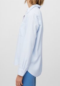 Light blue long-sleeve shirt with a collar, single chest pocket, buttoned cuffs, and a curved hemline; smooth fabric texture.