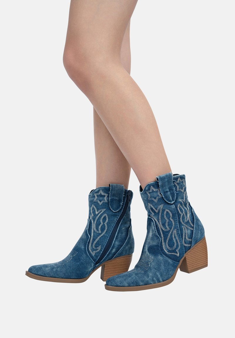 Botas de vaquero de jean azul con costura decorativa plateada, puntas afiladas, tacón apilado de altura media y cierre lateral con cremallera. Tejido texturizado.