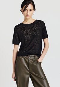 Maglione nero a maniche corte in maglia con motivo a diamante e colletto a costine, abbinato a pantaloni in ecopelle verde oliva a vita alta.