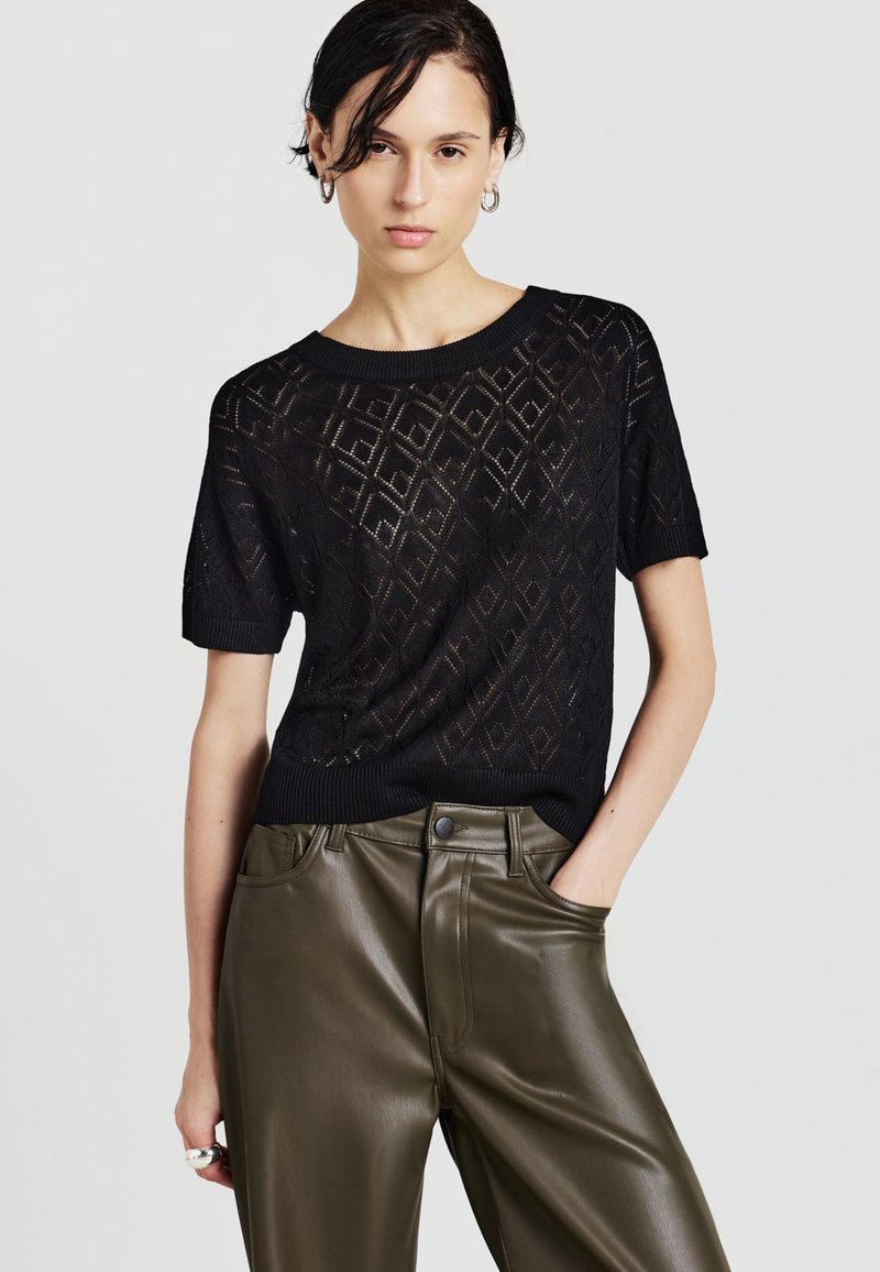 Maglione nero a maniche corte in maglia con motivo a diamante e colletto a costine, abbinato a pantaloni in ecopelle verde oliva a vita alta.