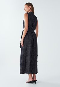 Czarna sukienka bez rękawów w białe kropki, z warstwowym fasonem i paskiem w talii. Wykonana z lekkiego materiału o gładkiej strukturze.