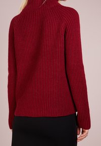 Pull bordeaux côtelé à col montant et manches longues, avec une coupe décontractée et un tissu texturé. L'ourlet arrive au niveau des hanches.