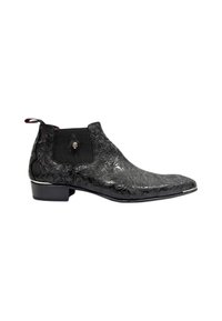 Bota de tobillo de cuero negro con diseño floral en relieve, panel lateral elástico texturizado y acento cromado a lo largo de la suela. Tacón bajo apilado.
