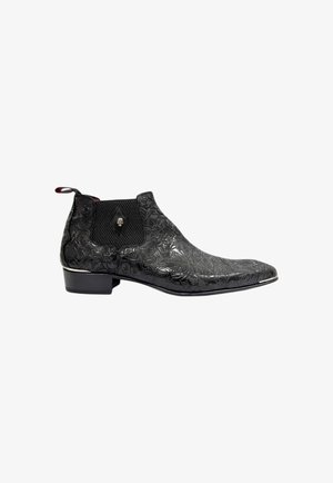 Black leather ankle boot with embossed floral design, textured elastic side panel, and chrome accent along the sole. Low stacked heel.