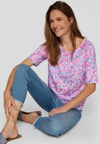 Short-sleeve blouse in pink and blue floral pattern, soft fabric, gathered neckline, paired with light blue jeans and flat sandals.