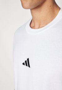 Witte katoenen T-shirt met een ronde hals. Voorzien van een zwart geborduurd logo met drie diagonale strepen op de linkerkant van de borst.