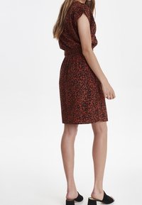 Röd och svart leopardmönstrad klänning med korta ärmar, elastisk midja och knälång fåll. Buren med svarta slip-on skor.