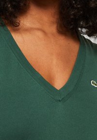 Grön v-ringad topp i ribbat tyg med en smal passform. Har en liten broderad logotyp på bröstet.