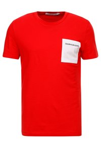 Czerwona koszulka z bawełny z okrągłym dekoltem, krótkimi rękawami i białą kieszonką na piersi z nadrukiem "CALVIN KLEIN JEANS" w czerni.